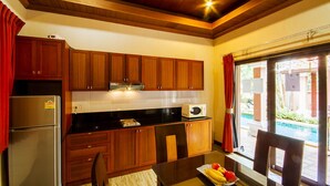 A kitchen with wooden cabinets, a refrigerator, a microwave, and a dining table with a fruit bowl.