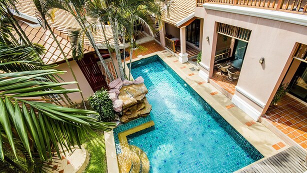 A swimming pool with a stone waterfall, surrounded by palm trees and a tiled deck.