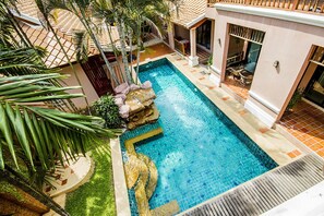 Ein Pool mit einem Steine Wasserfall, umgeben von Palmen und einer gefliesten Terrasse.