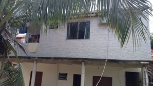 Un bâtiment à deux étages, doté d’une façade recouverte de tuiles, d’une fenêtre dont un carreau est cassé et d’un appareil de climatisation visible.