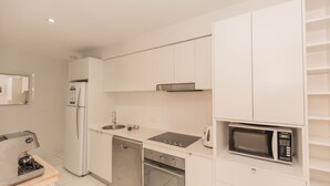 A modern kitchen with white cabinets, a stainless steel refrigerator, a dishwasher, an oven, a microwave, and a coffee machine.