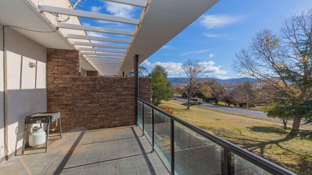 A balcony with a glass railing overlooking a road and trees.