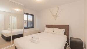 A bedroom with a large bed, a window, a mirror, and a wall-mounted deer head decoration.