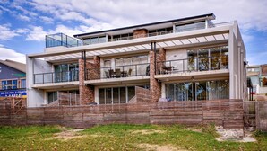 A modern two-story building with a flat roof, large windows, and a wooden fence in front.