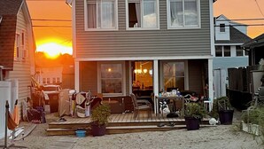 Een huis met twee verdiepingen, een veranda, een klein terras en een zandige voortuin.
