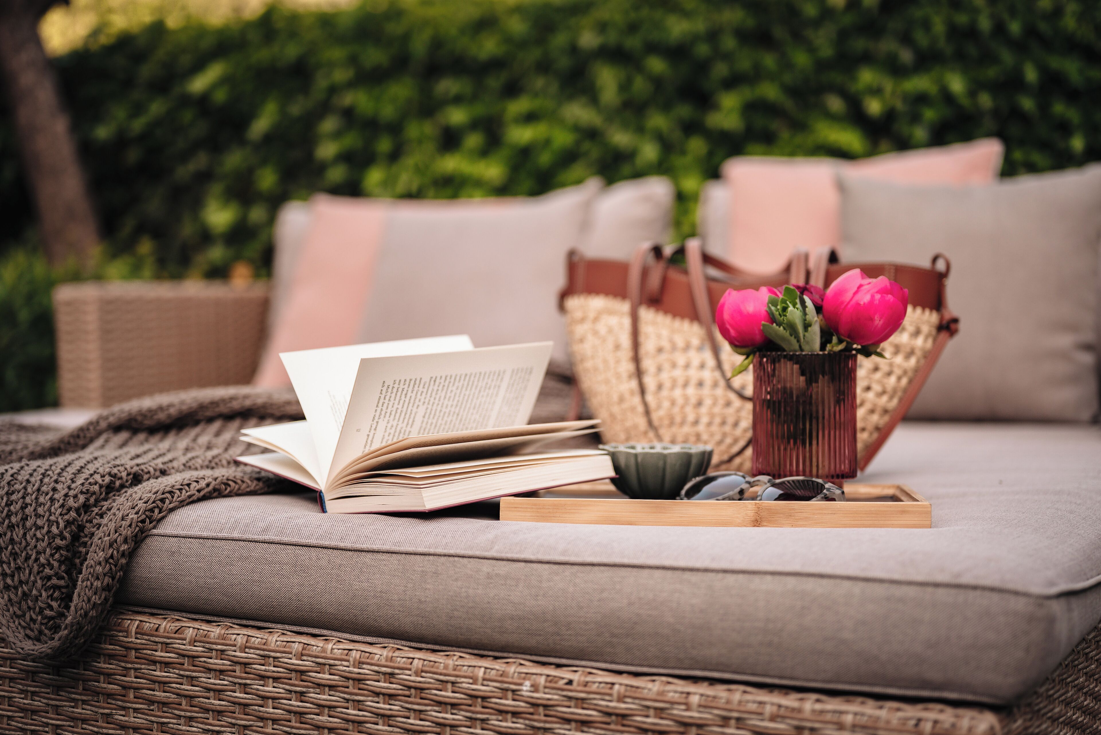 Ein Korbssessel mit einem Buch, einer Vase mit Blumen und einem Tablett mit Tasse und Steinen.