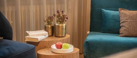 Une pièce chaleureuse avec un canapé de couleur turquoise, une table d’appoint en bois sur laquelle se trouvent un livre et un bol de fruits, et un radiateur dissimulé derrière des rideaux.