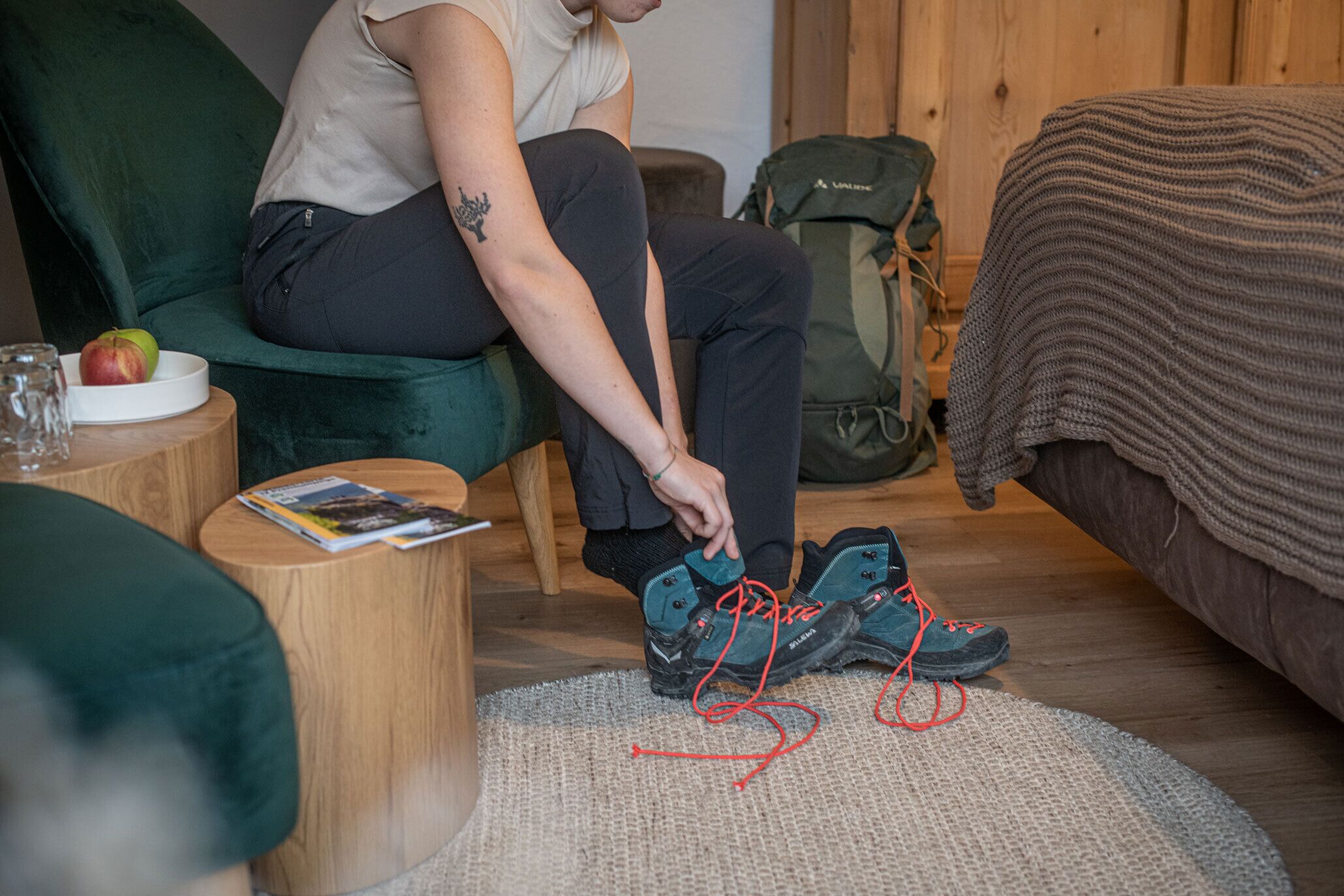 A person sitting on a green chair, tying shoelaces on a round rug.