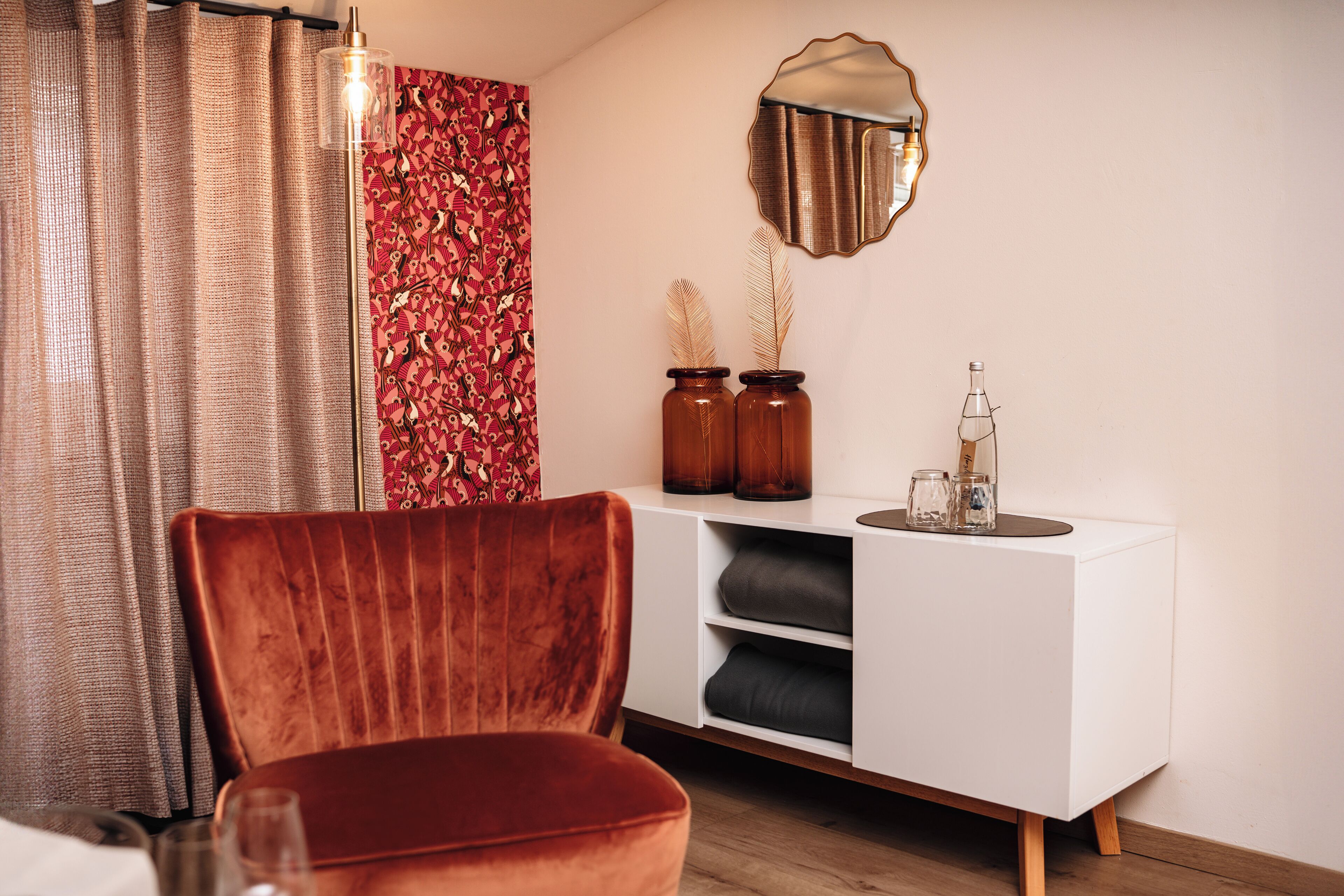 Un salón moderno con un sillón de terciopelo, un aparador blanco y un espejo decorativo.