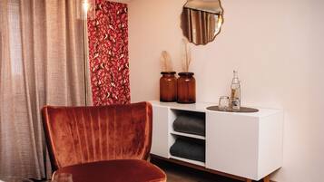 Un salón moderno con un sillón de terciopelo, un aparador blanco y un espejo decorativo.