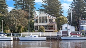 A waterfront property with a two-story house, docked boats, and a white fence. - Shearwater House - Riverfront Accommodation (Port Fairy)