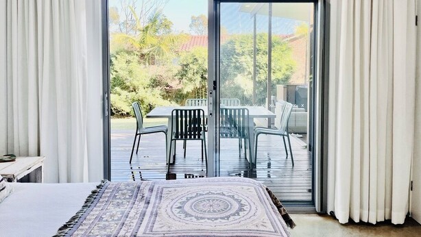 A bedroom with a large sliding glass door leading to an outdoor patio area with a table and chairs. - The Sea Life: 2 Min Walk to Beach + Private Outdoor Bath + Fireplace + Firepit (Manyana)
