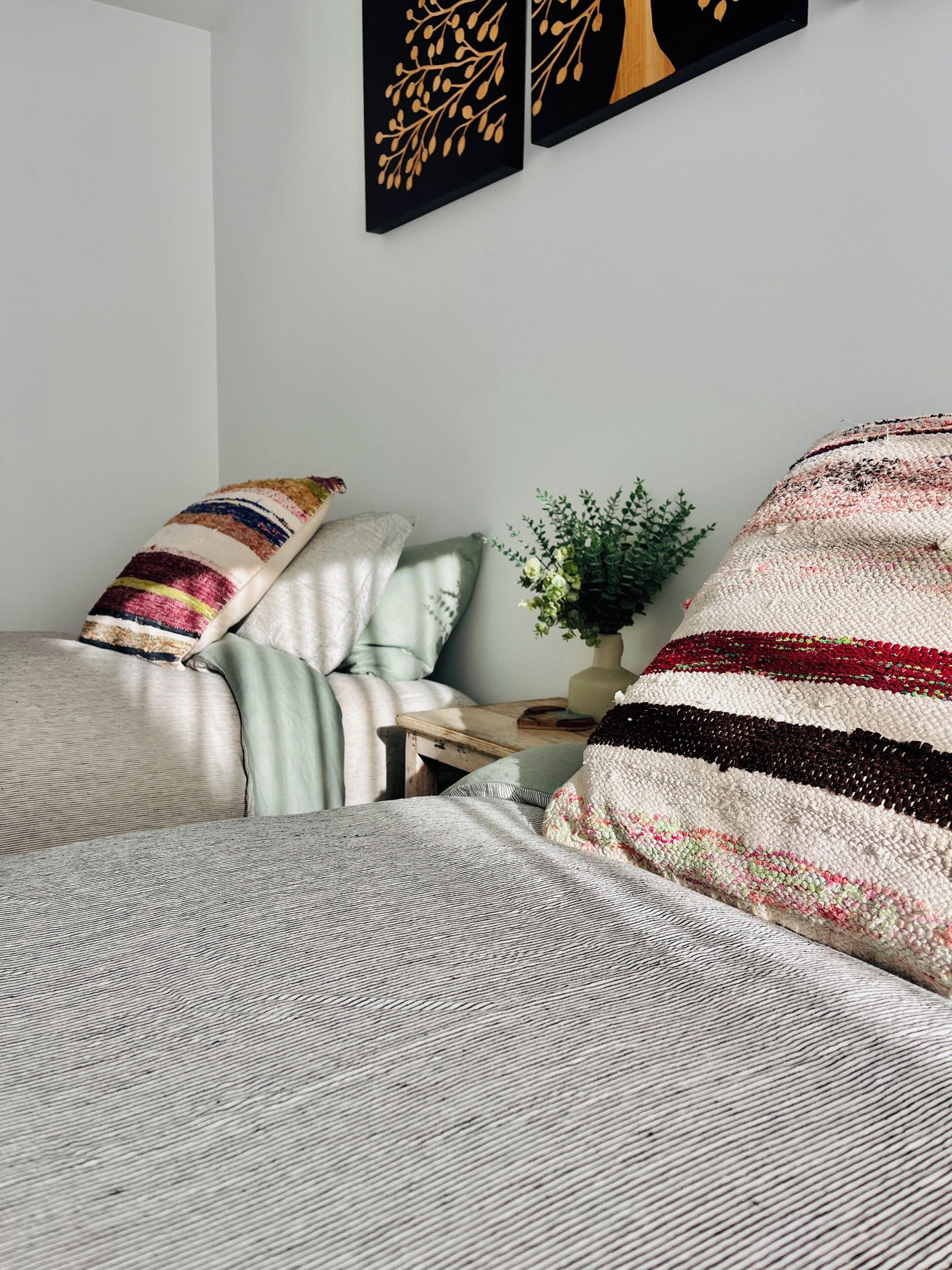 A neatly arranged bedroom with a bed, pillows, a bedside table with a plant, and two wall art pieces.