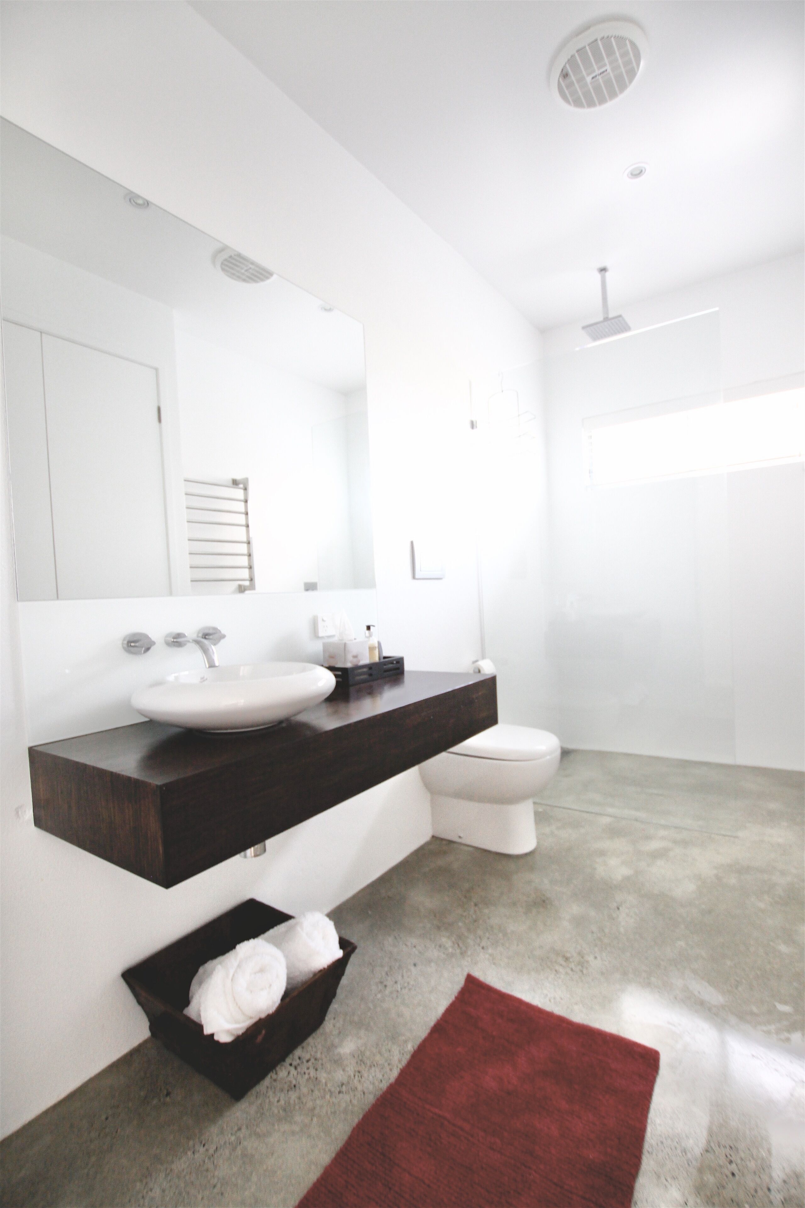 Un baño moderno con un lavamanos blanco, encimera oscura y una alfombra roja.