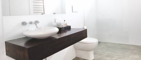 Un baño moderno con un lavamanos blanco, encimera oscura y una alfombra roja.