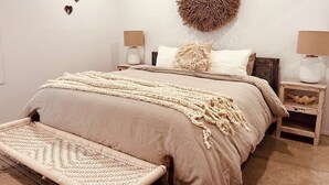 A bedroom with a large bed, two bedside tables, a wall-mounted circular decoration, and three heart-shaped wall art pieces. - The Sea Life: 2 Min Walk to Beach + Private Outdoor Bath + Fireplace + Firepit (Manyana)