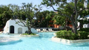 Ein Poolbereich mit einer kleinen weißen Struktur, umgeben von Bäumen und Liegestühlen.
