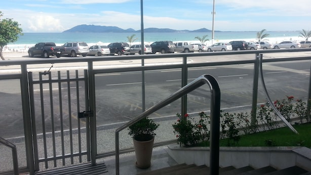 Une vue depuis un balcon donnant sur un parking rempli de véhicules, avec une plage en arrière-plan.