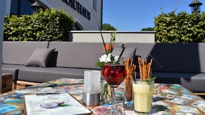 A table with a cocktail menu, a glass of red drink with berries, a glass of white drink, and a candle. - Hotel & Brauereigasthof Püttner (Schlammersdorf)