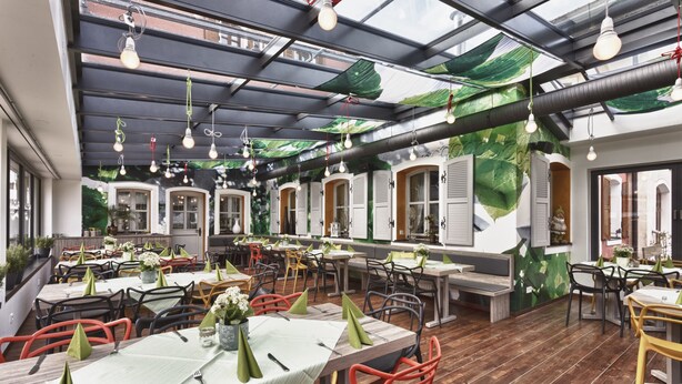 A restaurant with multiple tables and chairs, a wooden floor, and a ceiling with hanging lights. - Hotel & Brauereigasthof Püttner (Schlammersdorf)