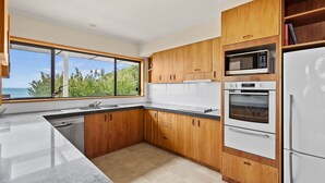 A modern kitchen with wooden cabinets, a built-in oven, microwave, and a large window offering a view of the ocean. - Beachfront - elevated ocean views (Port Fairy)