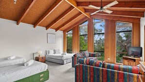 A spacious room with a high ceiling, wooden beams, a large window, a colorful sofa, a bed, and a television. - Beachfront - elevated ocean views (Port Fairy)