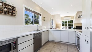 Une cuisine moderne avec des meubles blancs, un lave-vaisselle, un four encastré et une grande fenêtre donnant sur la verdure.
