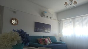Un soggiorno con un divano color petrolio, un condizionatore d'aria bianco, un lampadario e un quadro raffigurante un ponte.