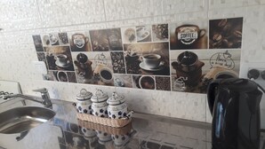 Cucina con zoccolo piastrellato che mostra foto e testo a tema caffè, lavello in acciaio inossidabile e macchina da caffè sul piano di lavoro.
