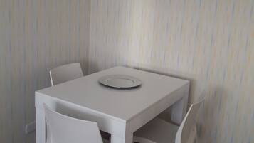 Una pequeña mesa de comedor blanca con cuatro sillas, un plato sobre la mesa y un fondo de papel tapiz a rayas.