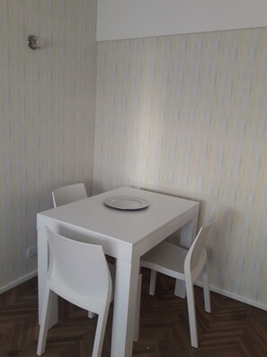 Et lille, hvidt spisebord med fire stole, en tallerken på bordet og tapet med striber i baggrunden.