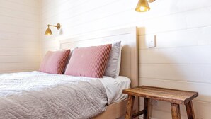 A bed with a quilted cover, two pillows, a bedside table, and a wall-mounted light fixture. - Kinsale Cottage - perfect central location (Port Fairy)