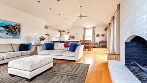 A spacious living room with a fireplace, a dining area, and a kitchen in the background. - Kinsale Cottage - perfect central location (Port Fairy)