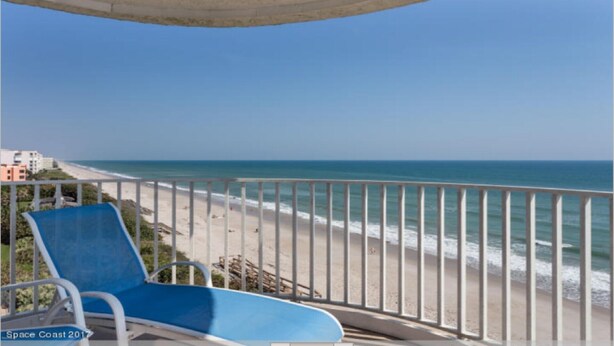 Un balcón con una silla azul que da a la playa.