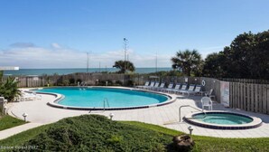 Un área de piscina con una gran piscina ovalada, jacuzzis circulares más pequeños y sillones de descanso.