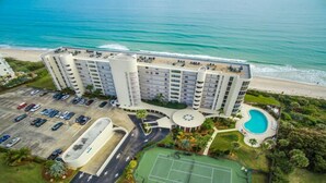 Un gran hotel con varias plantas, un estacionamiento, una piscina y una cancha de tenis.