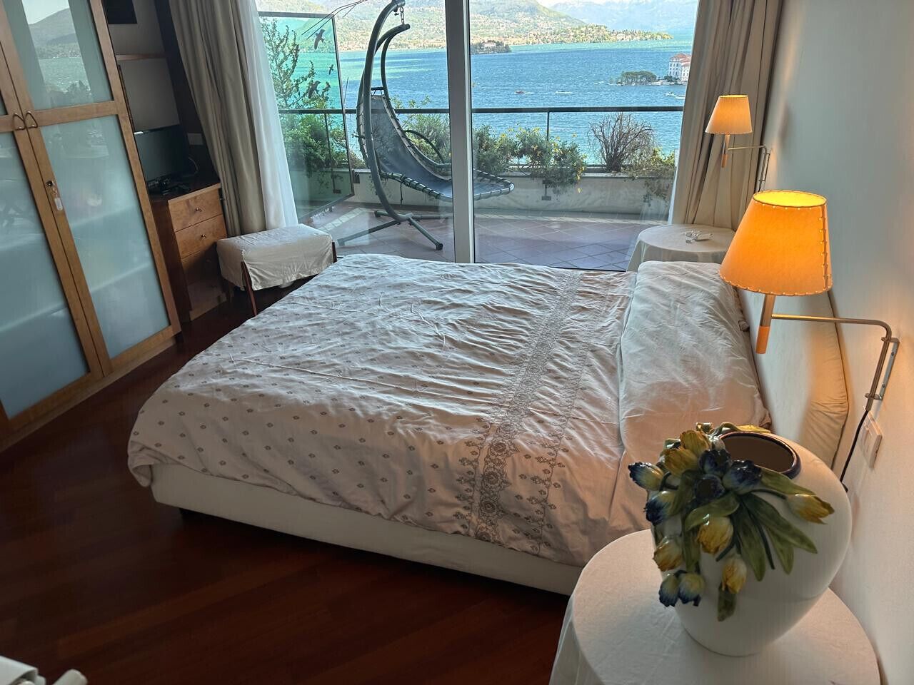Un dormitorio con cama, mesita de noche con lámpara, una silla y vista al mar.