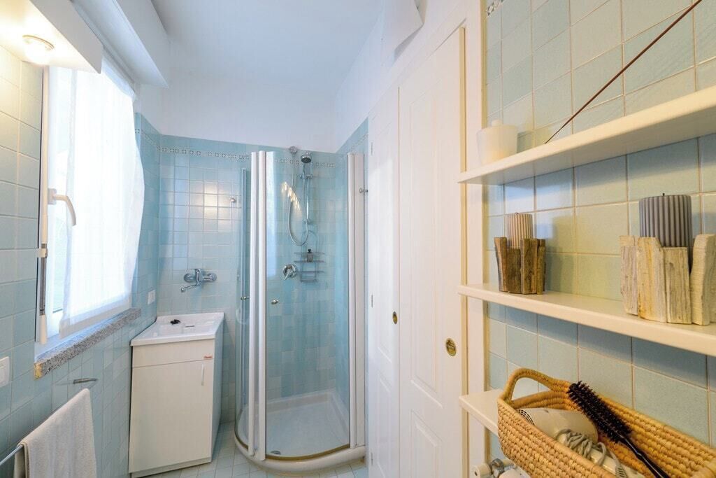 Un baño con ducha de vidrio, lavamanos y estante con artículos de aseo.