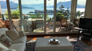 Una sala de estar con sofá, reposapiés y sillones, una televisión, y vistas a un lago y montañas a través de amplias ventanas.
