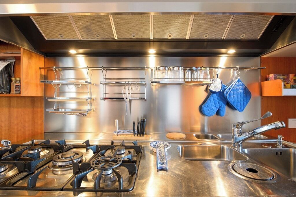 A modern kitchen with stainless steel appliances, a gas stove, a sink, and hanging utensils.