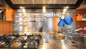 Una cocina moderna con electrodomésticos de acero inoxidable, estufa a gas, un lavabo y utensilios colgantes.