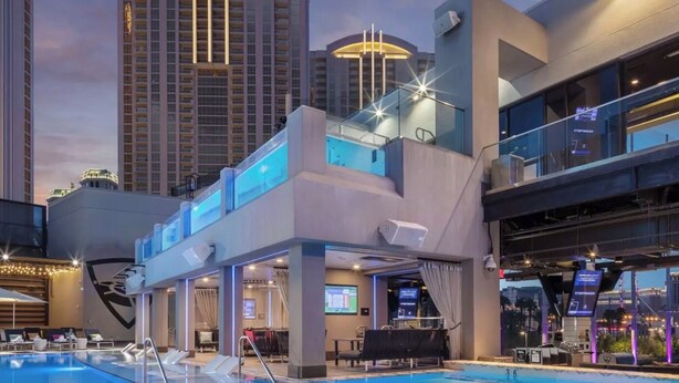 A modern hotel with a rooftop pool area, featuring a large pool with a geometric design, a lounge area with seating, and a view of surrounding high-rise buildings. - True 1BR  Strip View at MGM Signature (Las Vegas)