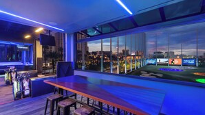 A modern bar area with a city view, a pool table, and golf bags. - True 1BR  Strip View at MGM Signature (Las Vegas)