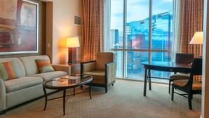 A hotel room with a large window, a sofa, a chair, a small table, and a lamp. - True 1BR  Strip View at MGM Signature (Las Vegas)