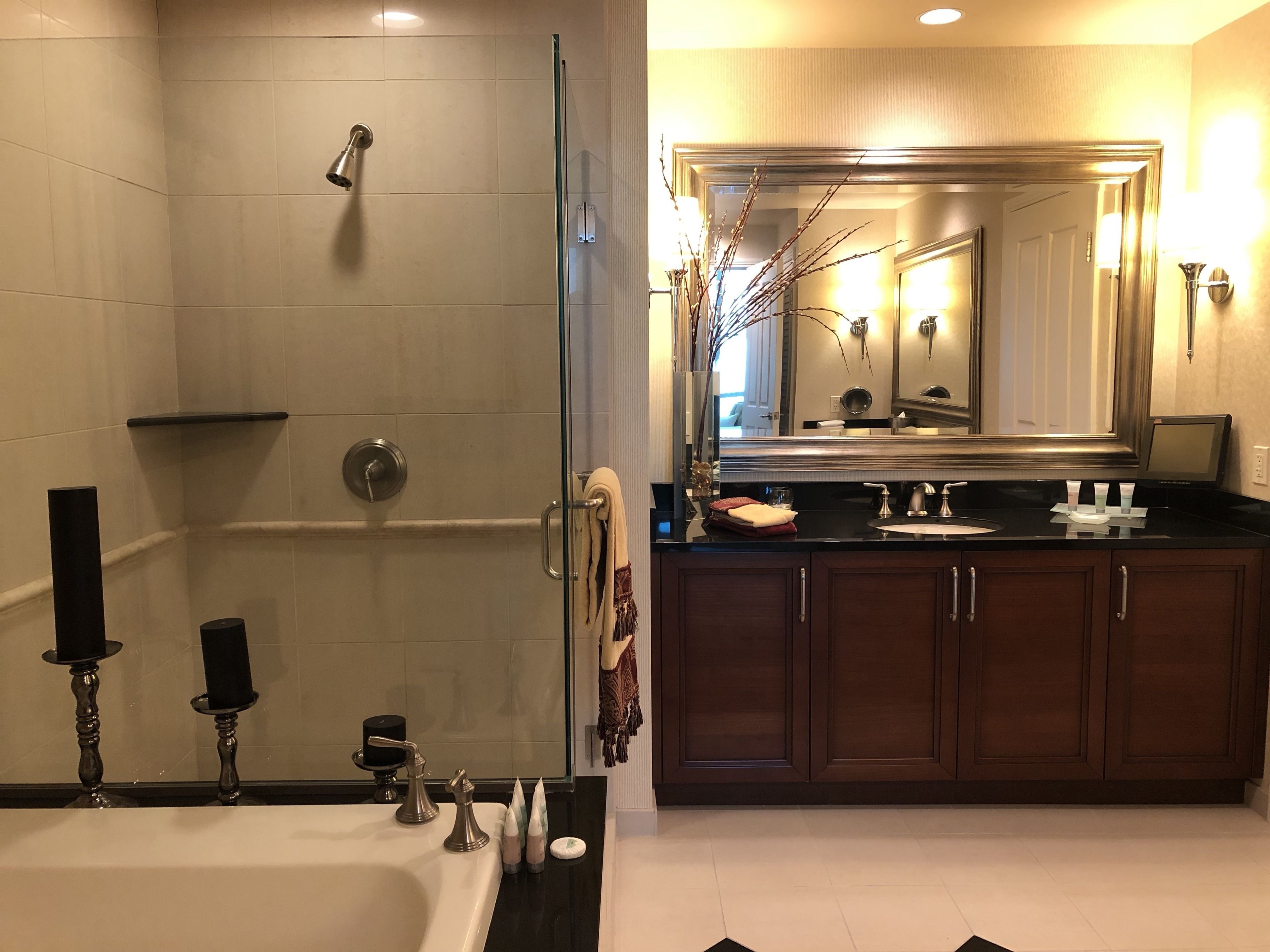 A modern bathroom with a glass-enclosed shower, a large mirror, and a vanity with a sink and multiple toiletries.