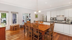 A modern kitchen with white cabinets, a wooden dining table, and a chandelier.