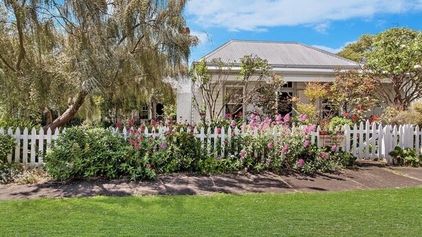 A house with a white picket fence, surrounded by lush greenery and flowering plants.