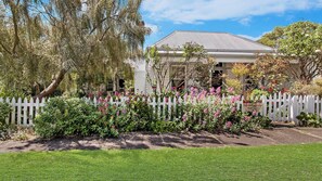 A house with a white picket fence, surrounded by lush greenery and flowering plants.