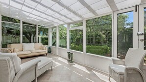 A sunlit covered patio with a sofa, chairs, and a decorative urn.