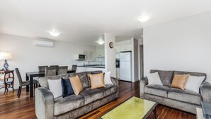 A modern living room with two grey sofas, a dining table, and a kitchen in the background. - The Moorings - Absolute River Frontage (Port Fairy)